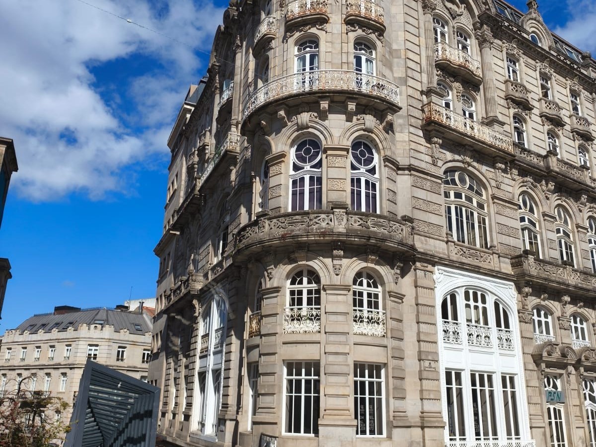 Ornate historic building with arched windows, corner view, blue sky and clouds in background.