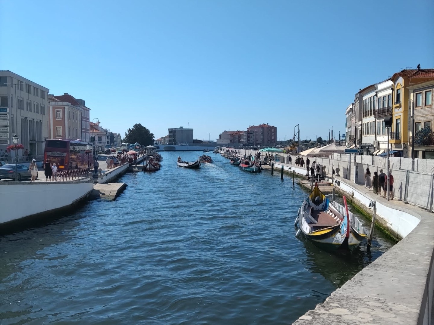 Sunny canal with boats, lined by colorful buildings and a clear blue sky overhead.