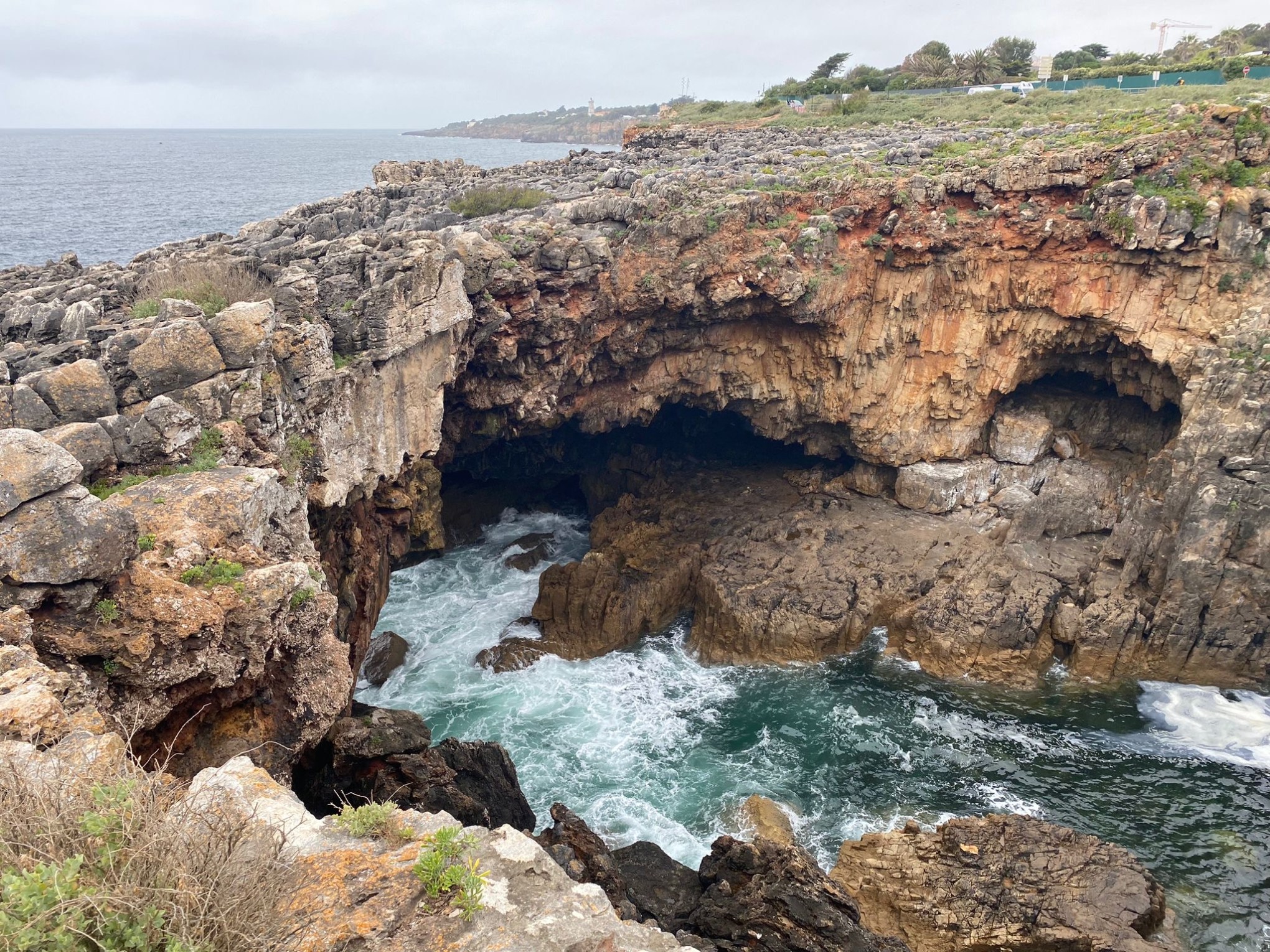 Rocky coastal cliff with a natural arch and ocean waves below on a cloudy day.